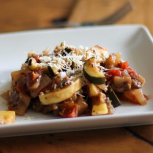 Ratatouille on a plate sitting on a wooden table, ready to eat.
