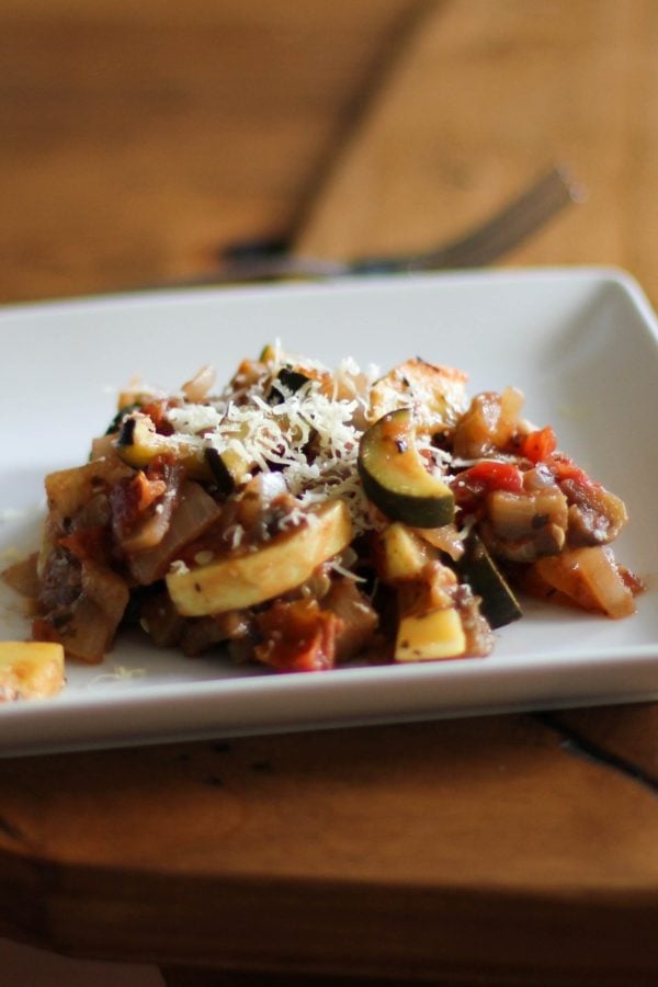 Ratatouille on a plate sitting on a wooden table, ready to eat.
