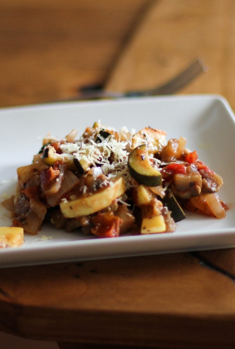 Ratatouille on a plate sitting on a wooden table, ready to eat.