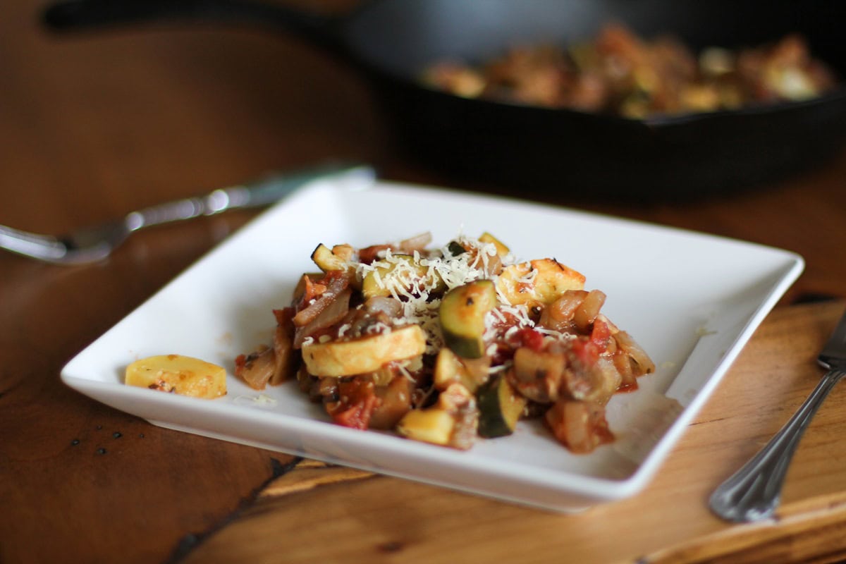 Ratatouille on a plate with a fork to the side and a skillet in the background.