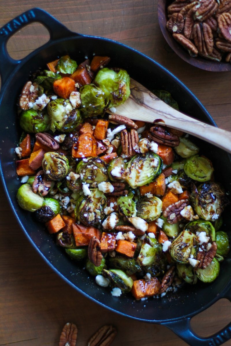 large cast iron baking dish filled with roasted brussels sprouts, sweet potatoes, pecans, feta cheese, and a balsamic drizzle. Ready to serve.
