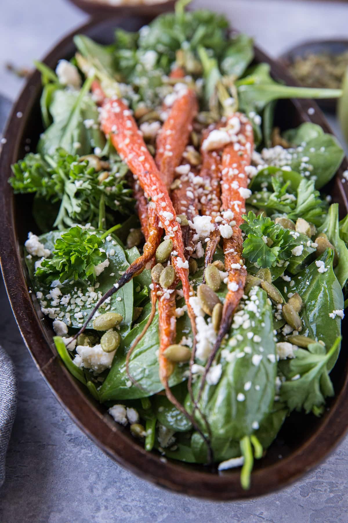 large wooden serving bowl full of spinach and carrot salad.
