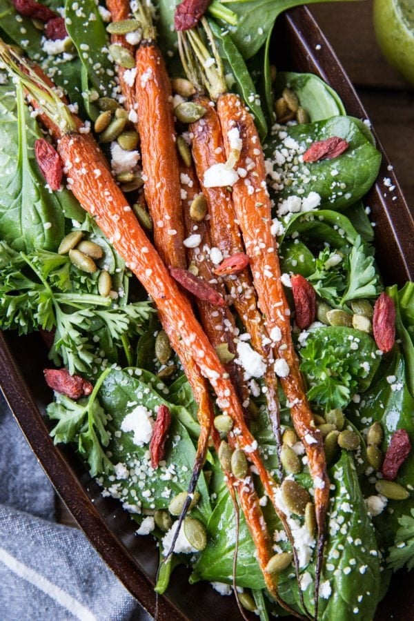 Roasted Carrot Spinach Salad with Lemon Herb Dressing in a large serving bowl. Roasted pumpkin seeds, feta cheese, and goji berries sprinkled on top
