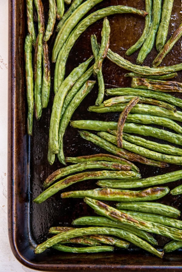 Roasted green beans on a large baking sheet fresh out of the oven with golden brown color.