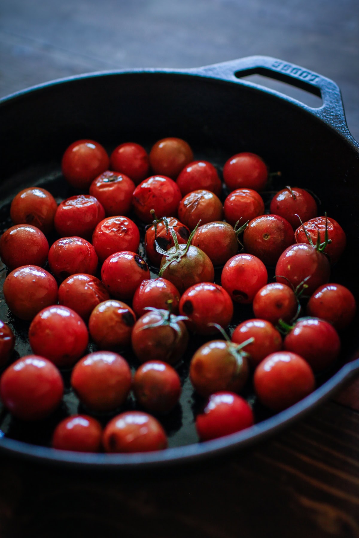 Large cast iron skillet full of cherry tomatoes, cooking to soften up.