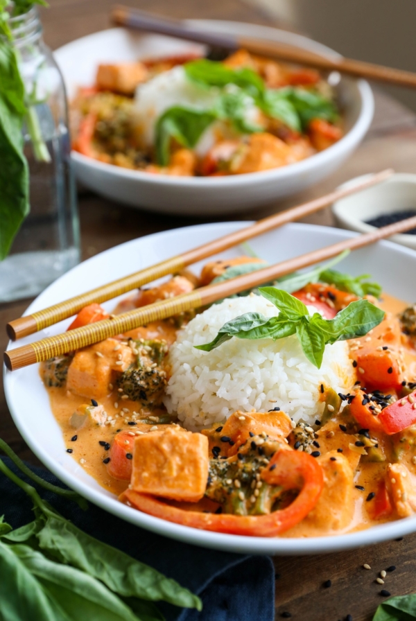 Two bowls of salmon curry with scoops of rice in the center and fresh basil all around. Chop sticks and a blue napkin for serving.