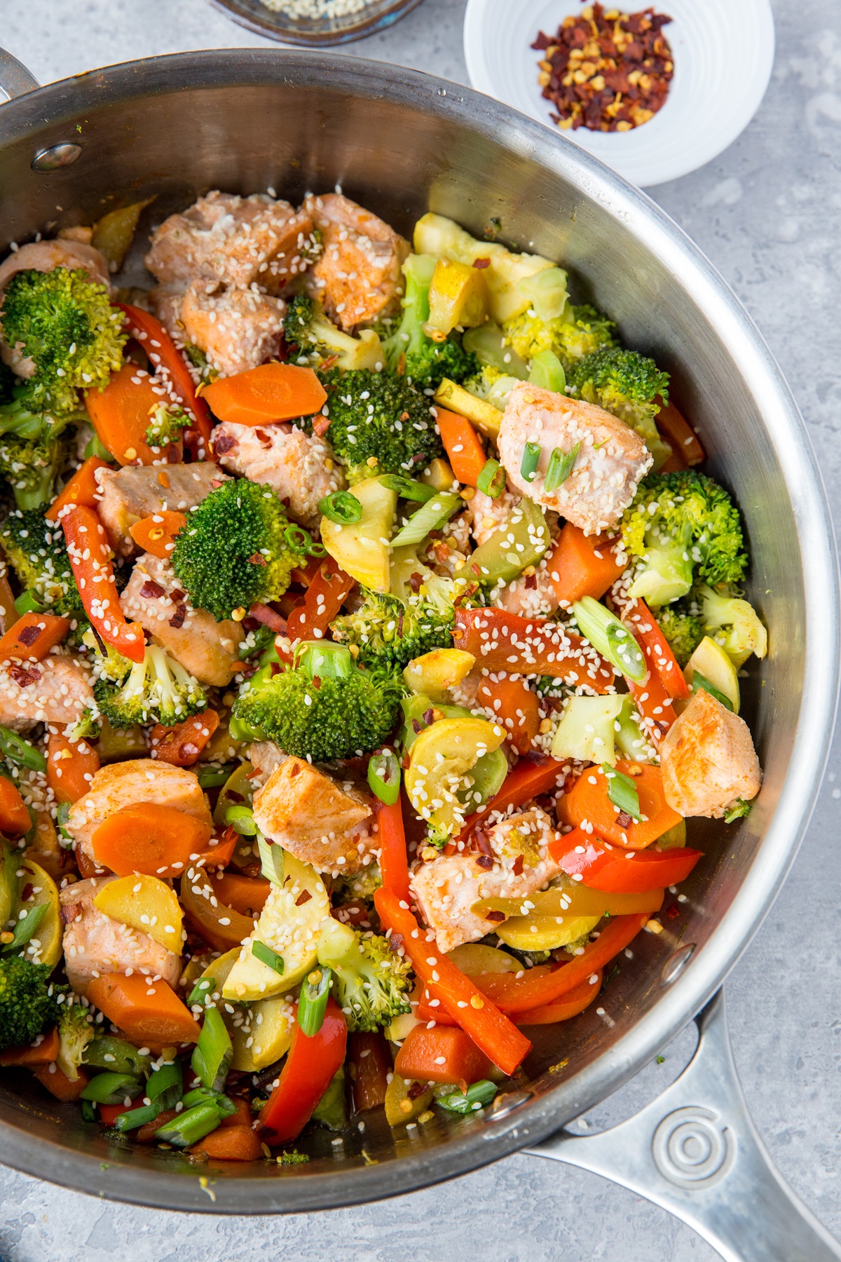 Stainless steel skillet with finished stir-fry salmon and vegetables, ready to consume.