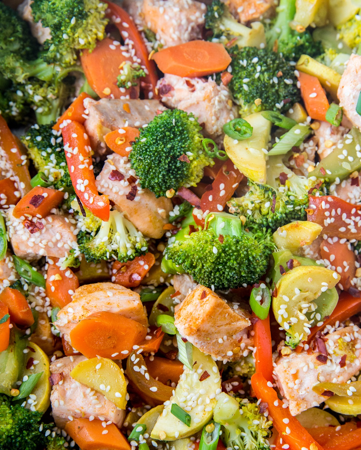 Closeup image of salmon stir fry in a skillet, sprinkled with sesame seeds, green onions, and red pepper flakes.