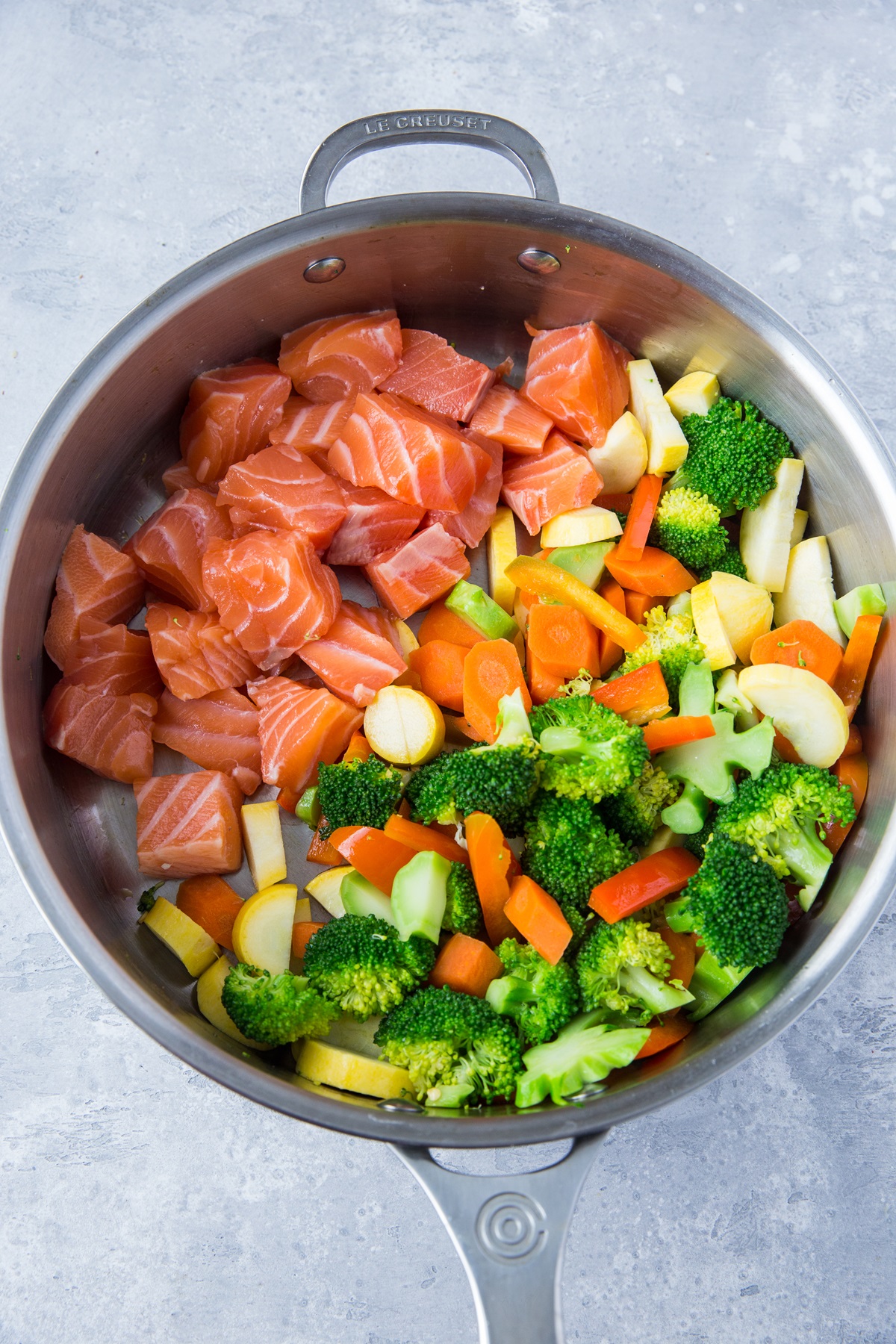 Raw chopped salmon pieces and chopped vegetables in a skillet to make salmon stir fry.