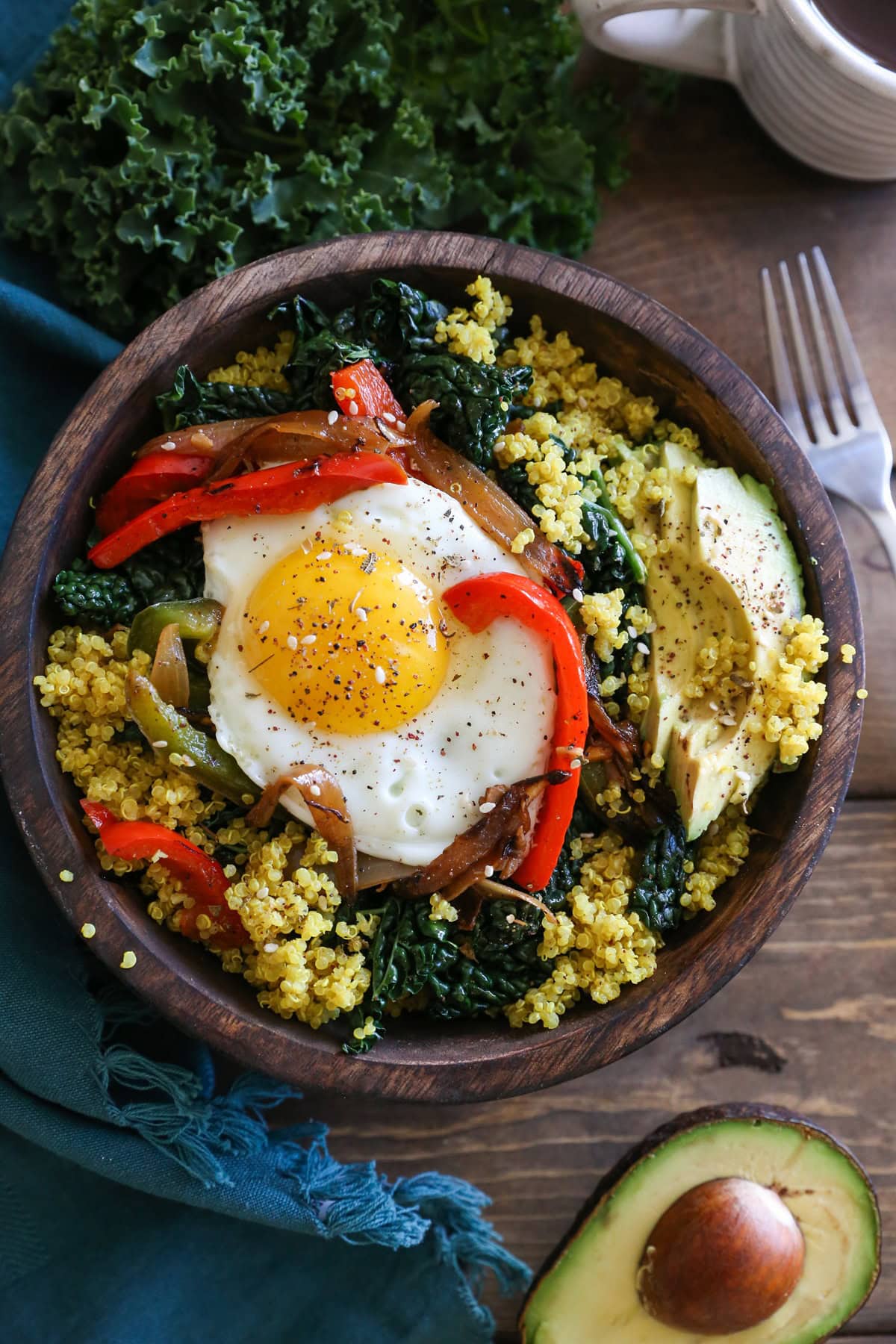 Wooden bowl full of turmeric quinoa with sauteed vegetables, a sunny side up egg and half of an avocado.