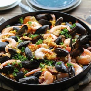 Seafood paella in a large paella pan, sprinkled with fresh parsley and ready to serve.