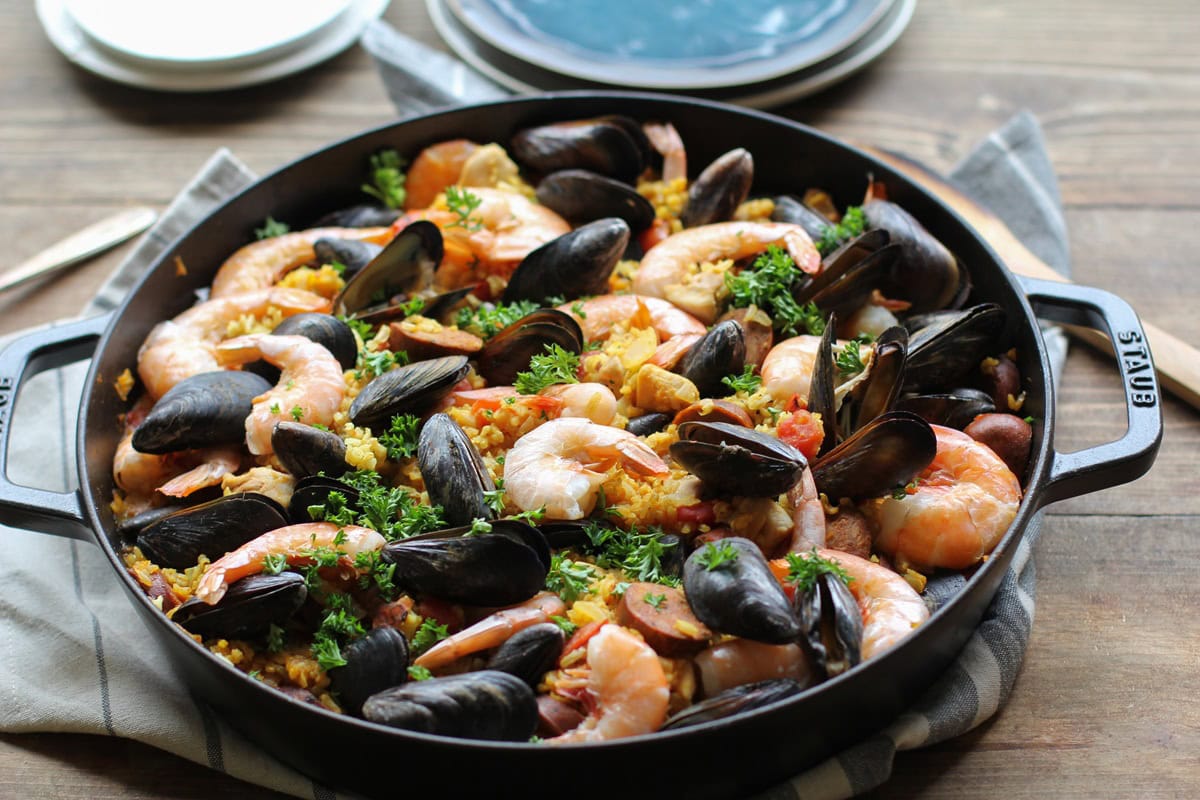 Seafood paella in a large paella pan, sprinkled with fresh parsley and ready to serve.