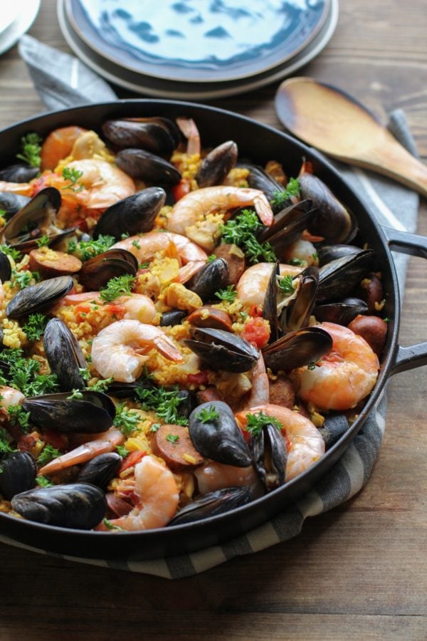 Large paella pan full of seafood paella with some plates ands serving spoons in the background, ready to be served.