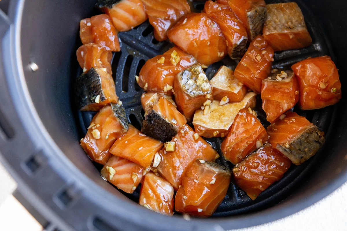 Raw marinated salmon cubes in an air fryer, ready to air fry.