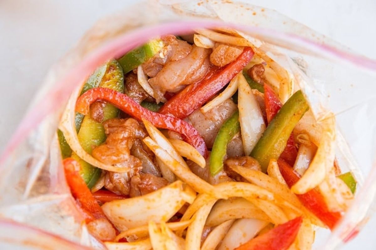 large zip lock bag full of marinated chicken, onions, and bell peppers for chicken fajitas.