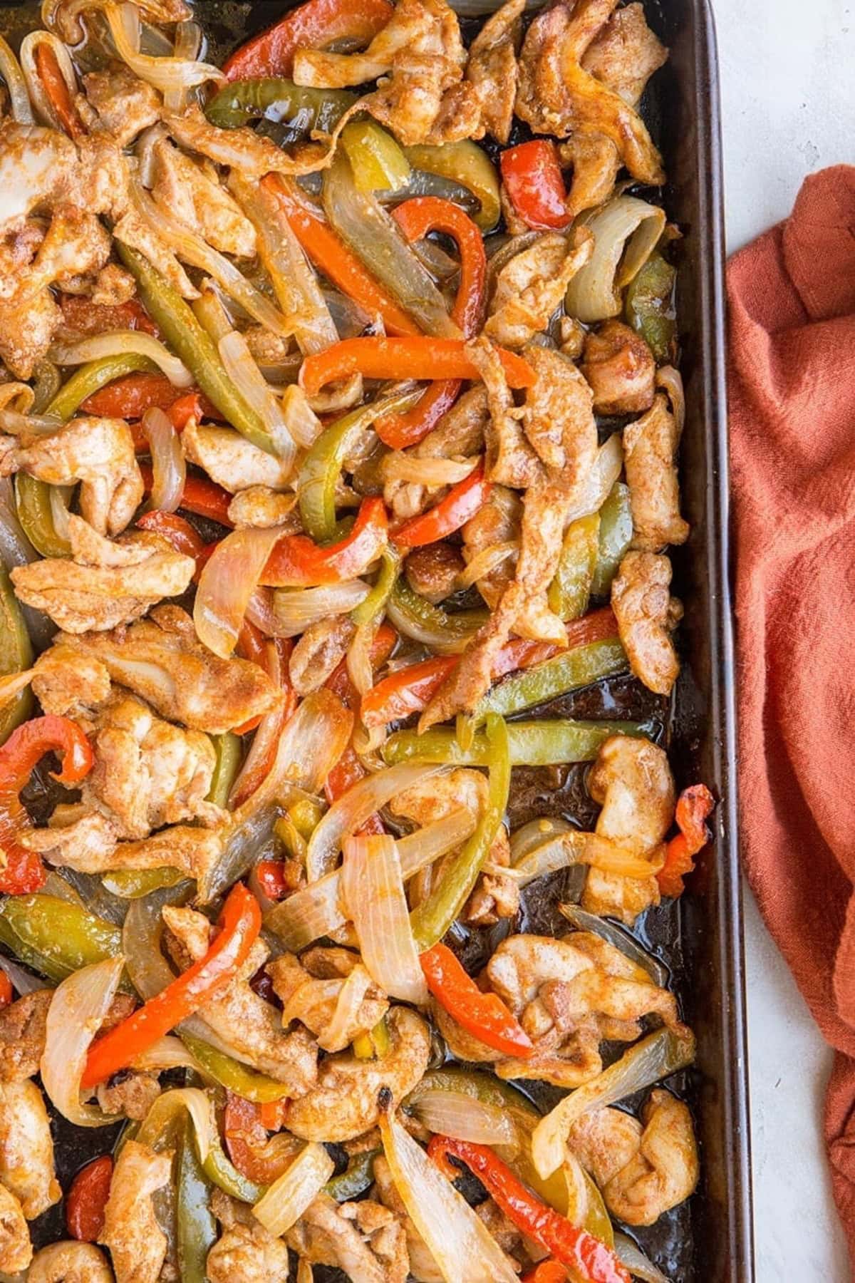 Rimmed baking sheet with chicken fajitas on top and a red napkin to the side. Fresh out of the oven and ready to serve.