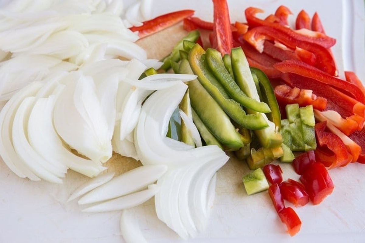 Sliced onions and bell peppers on a cutting board.