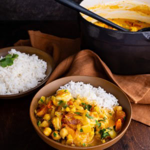 Shrimp curry in a brown ceramic bowl with the pot of the rest of the curry in the background.