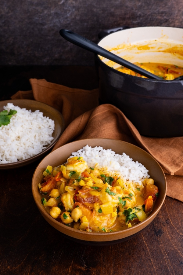 Shrimp curry in a brown ceramic bowl with the pot of the rest of the curry in the background.