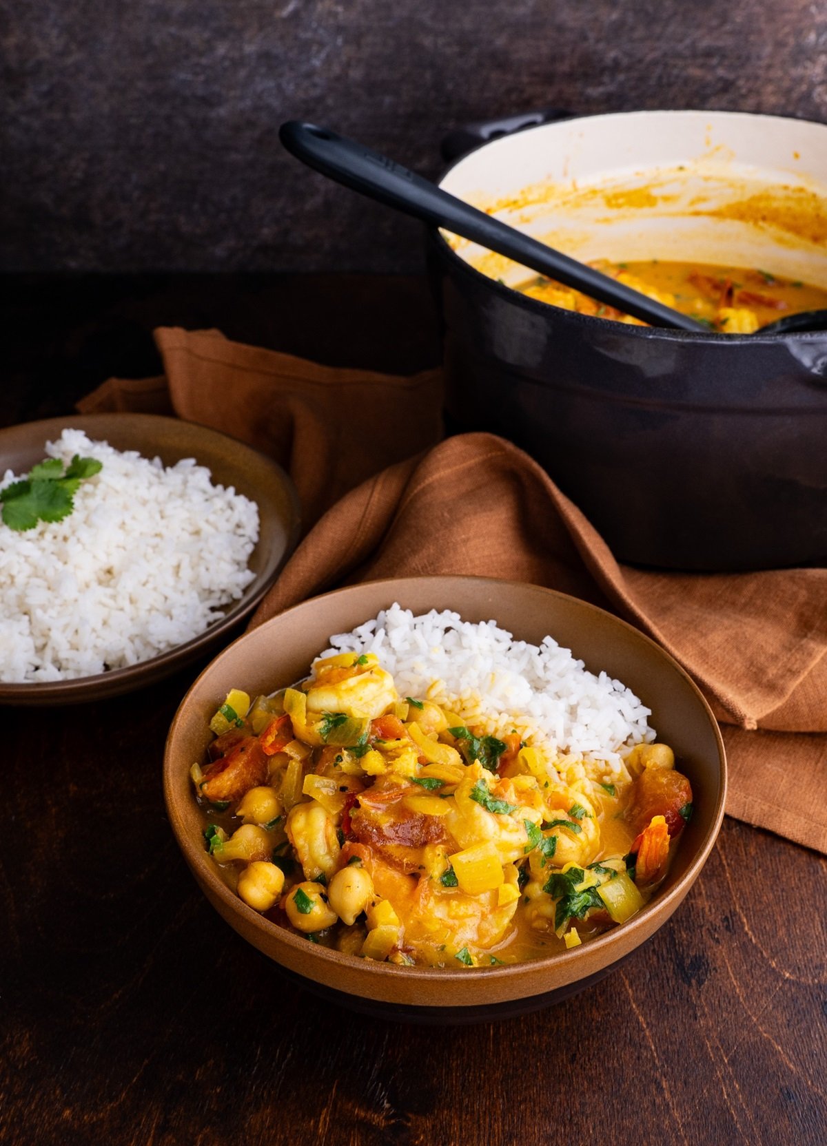 Shrimp curry in a brown ceramic bowl with the pot of the rest of the curry in the background.