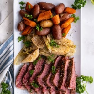 White platter of sliced corned beef, cabbage, and potatoes on a marble surface.