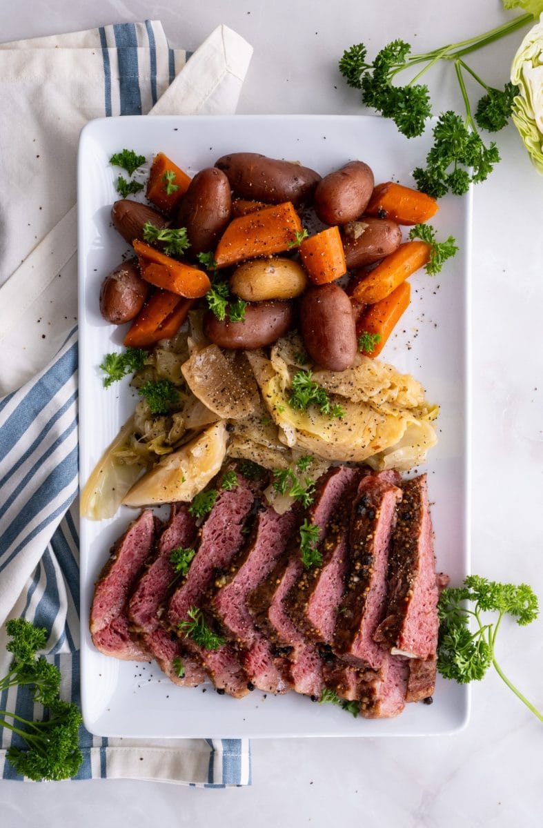 White platter of sliced corned beef, cabbage, and potatoes on a marble surface.