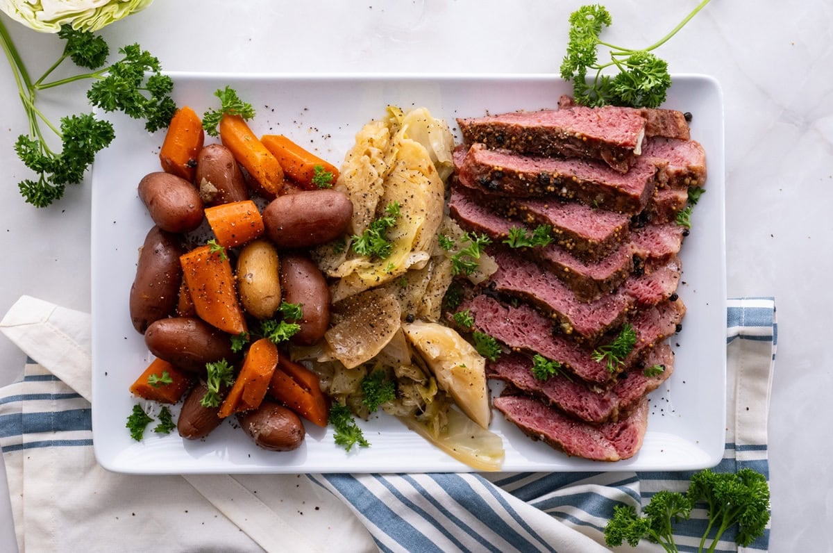 Marble table with a platter of corned beef and cabbage and fresh parsley to the side, ready to serve.