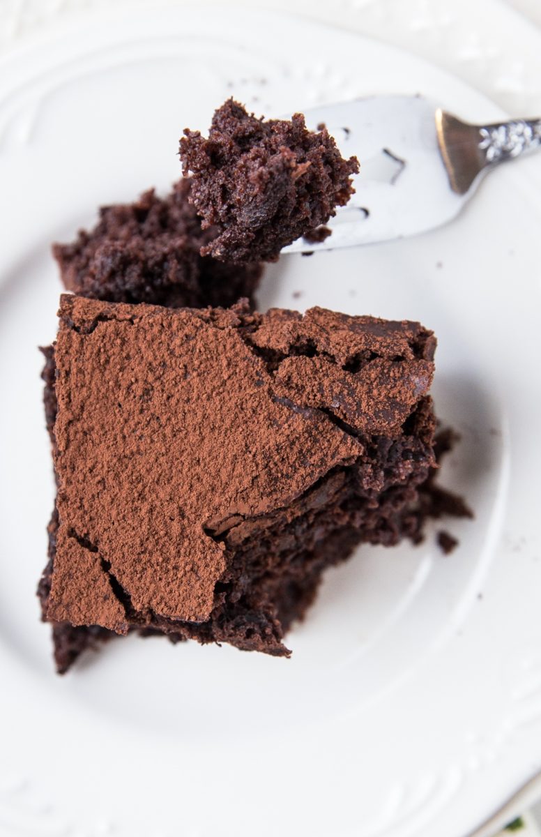 Slice of sourdough chocolate cake on a white plate with a fork taking a bite out.