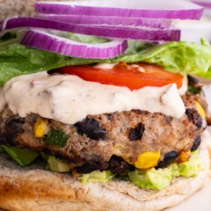 Close up image of a turkey burger on a plate with chipotle yogurt sauce, onion, tomato, and lettuce, ready to eat.