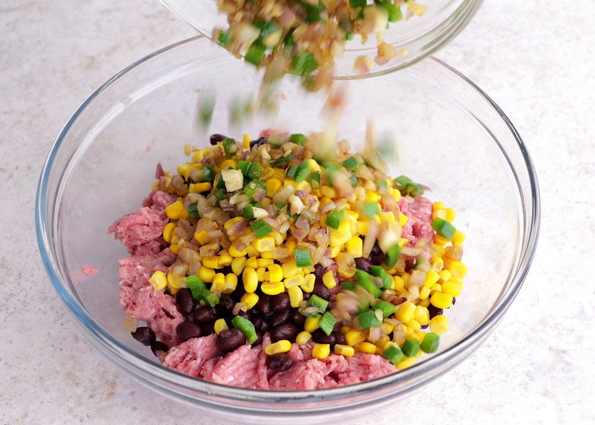 Raw ground turkey meat in a mixing bowl with beans, corn, onion, jalapenos, ready to be mixed into the burger meat.