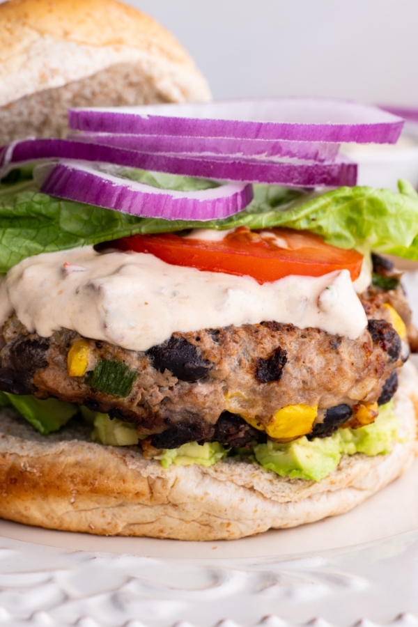 Close up image of a turkey burger on a plate with chipotle yogurt sauce, onion, tomato, and lettuce, ready to eat.