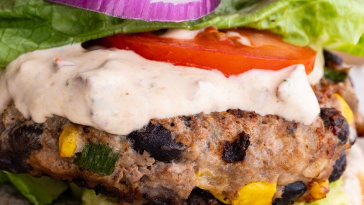 Close up image of a turkey burger on a plate with chipotle yogurt sauce, onion, tomato, and lettuce, ready to eat.