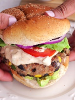 Hands holding a turkey burger with chipotle sauce and burger toppings.