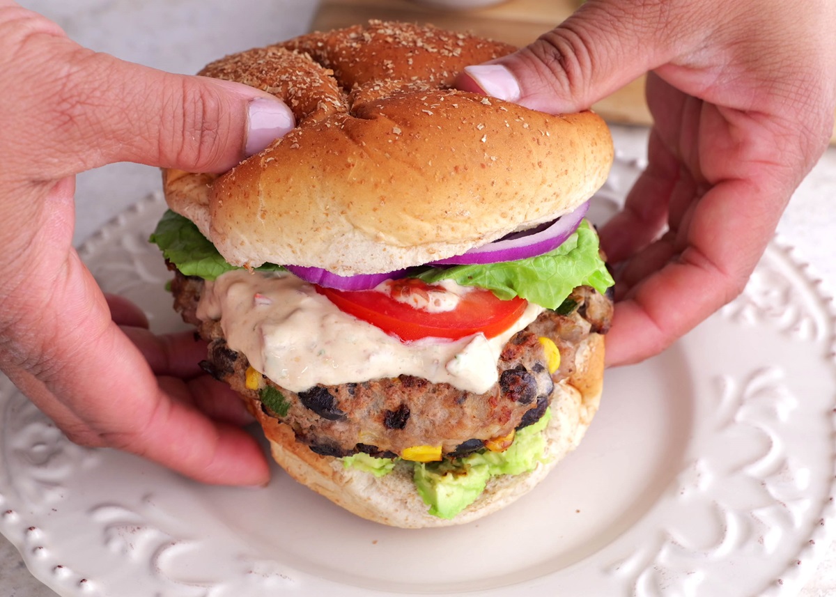 Hands holding a turkey burger with chipotle sauce and burger toppings.