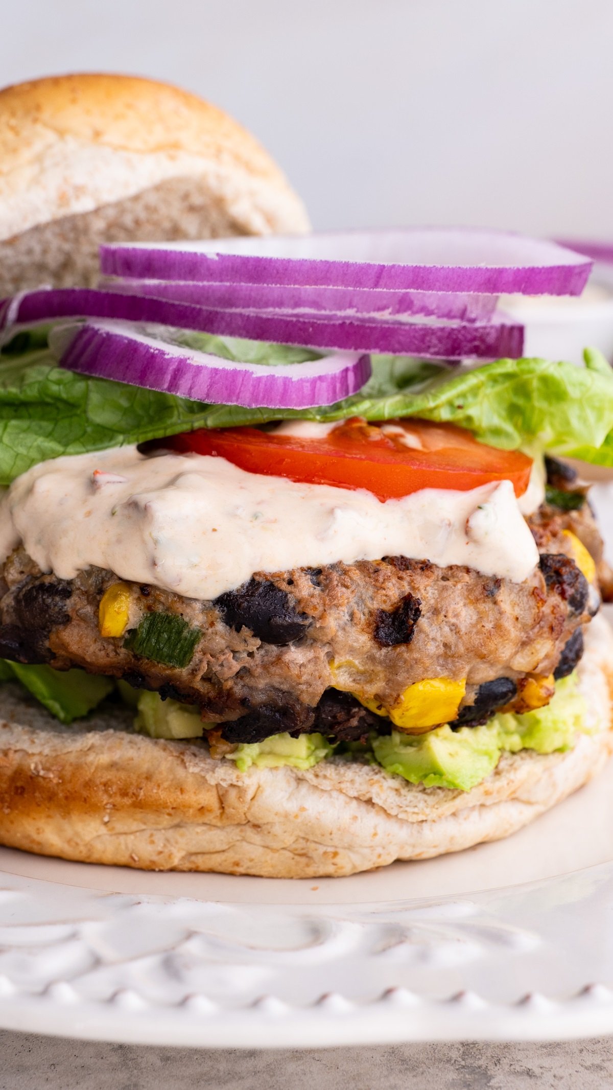 Close up image of a turkey burger on a plate with chipotle yogurt sauce, onion, tomato, and lettuce, ready to eat.