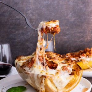 Spaghetti Squash Lasagna Boats on a plate with a fork pulling some of the cheese off.