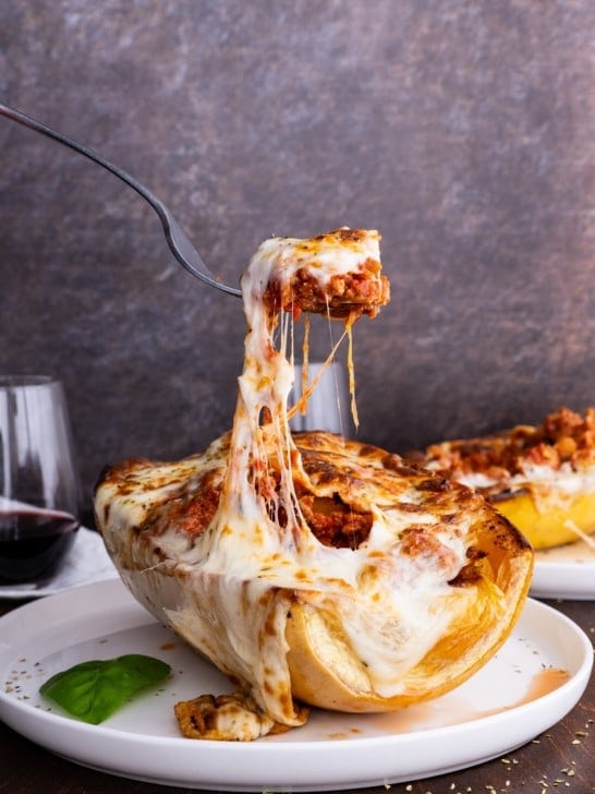 Spaghetti Squash Lasagna Boats on a plate with a fork pulling some of the cheese off.