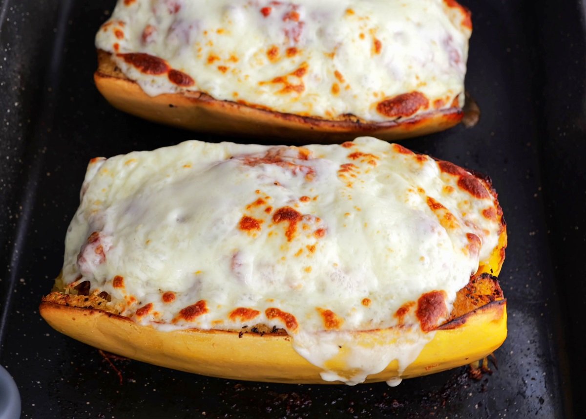 Two spaghetti squash halves on a baking dish stuffed with bolognese sauce and covered with melted cheese.