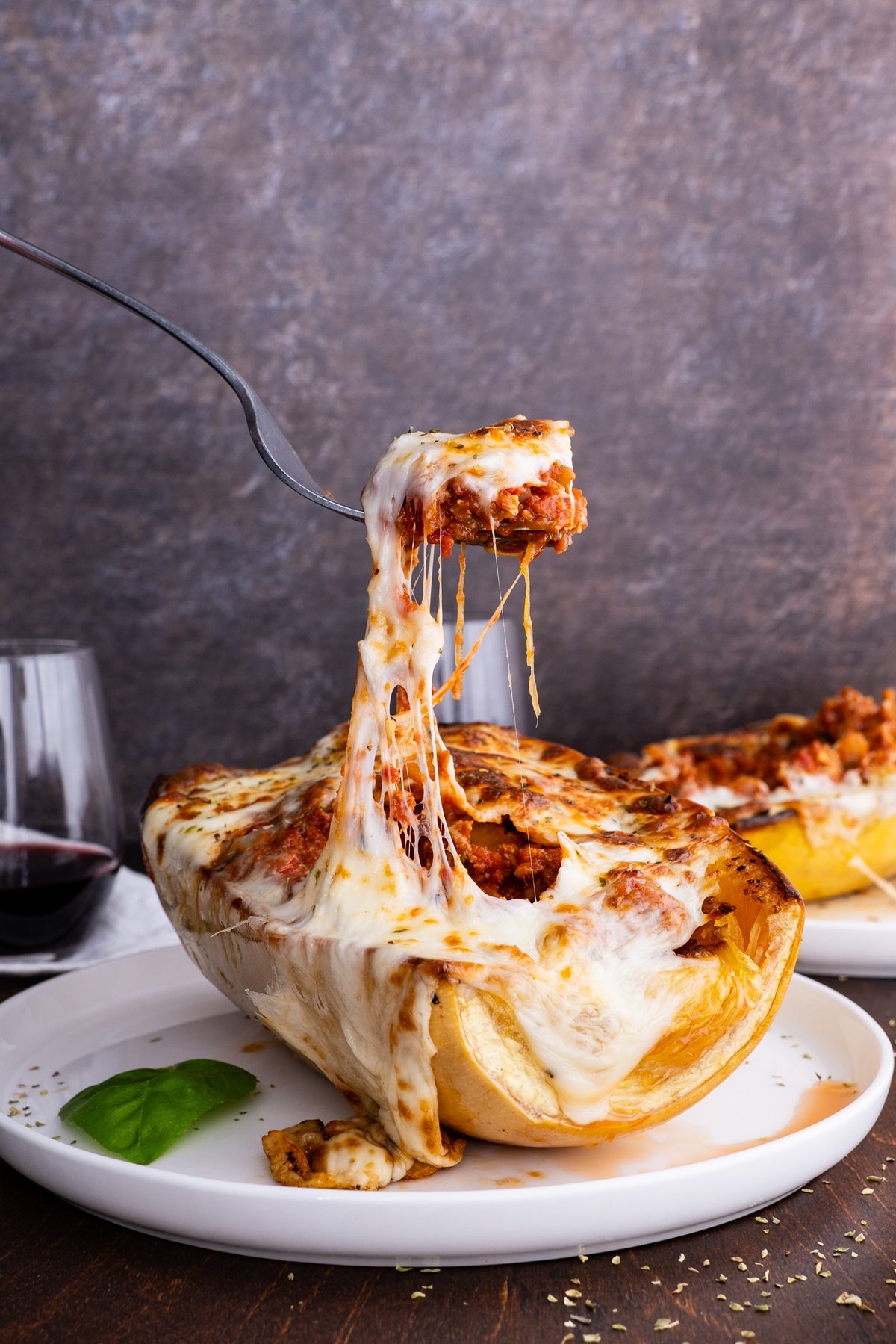 Spaghetti Squash Lasagna Boats on a plate with a fork pulling some of the cheese off.