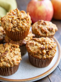 Plate of spiced apple carrot muffins with fresh apples in the background, ready to eat.