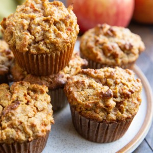 Plate of spiced apple carrot muffins with fresh apples in the background, ready to eat.
