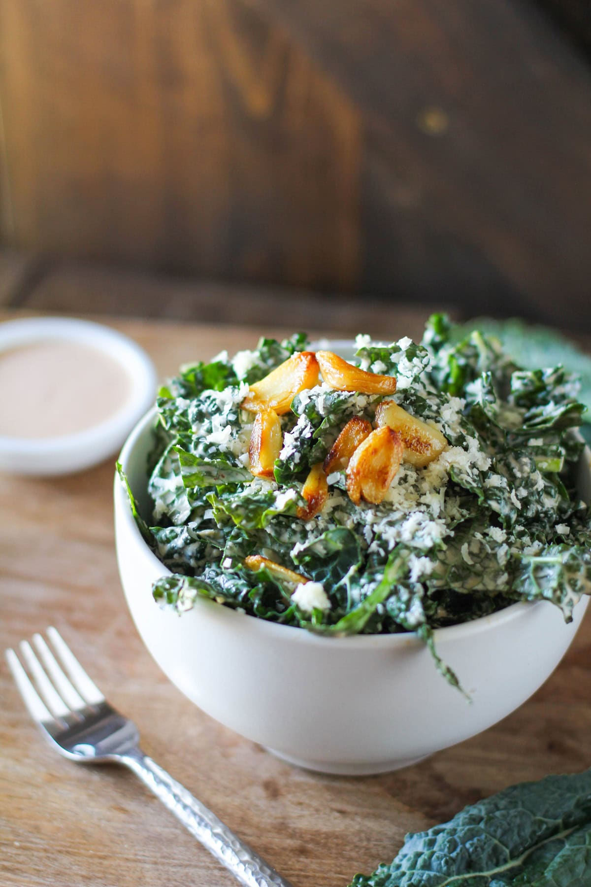 caesar salad in a white bowl with roasted garlic on top and a silver fork to the side.