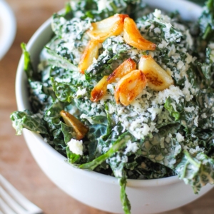 Spicy Kale Caesar Salad with Roasted Garlic in a large white bowl with a fork to the side and roasted garlic on top, ready to eat