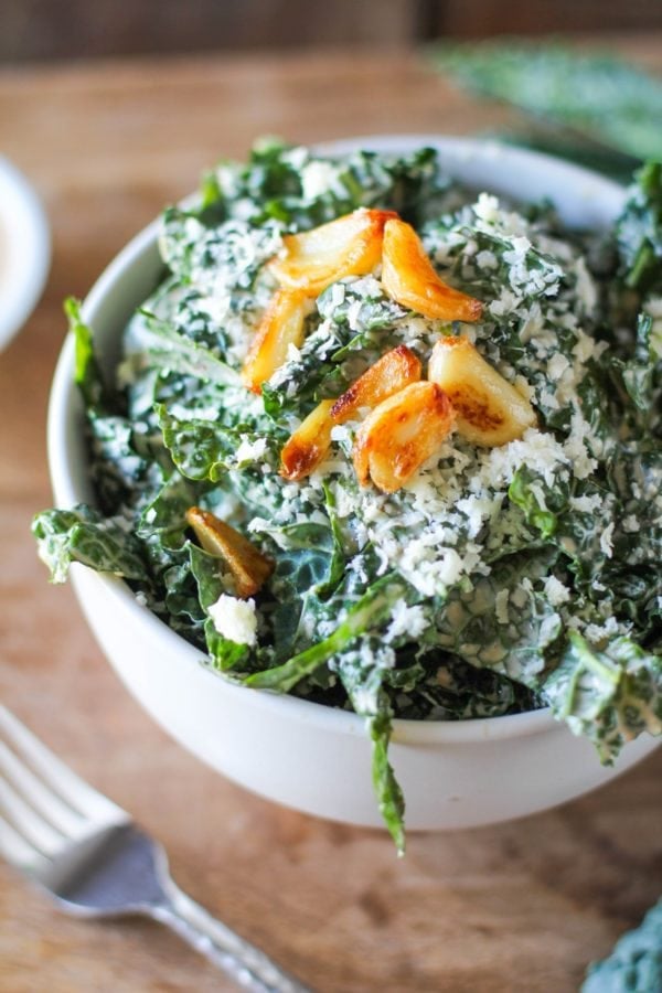Spicy Kale Caesar Salad with Roasted Garlic in a large white bowl with a fork to the side and roasted garlic on top, ready to eat