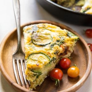 Slice of Spinach Frittata with Zucchini, Sun-Dried Tomatoes, and Goat Cheese on a plate with the rest of the frittata in the background.