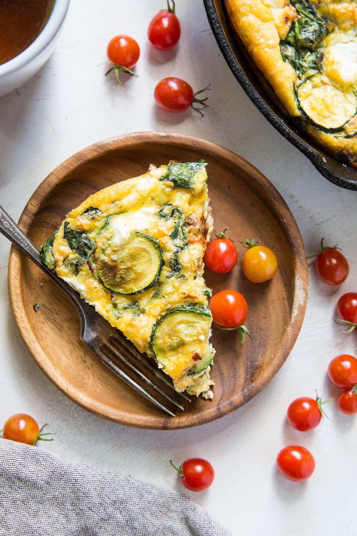 Spinach Frittata on a wooden plate with fresh cherry tomatoes around.