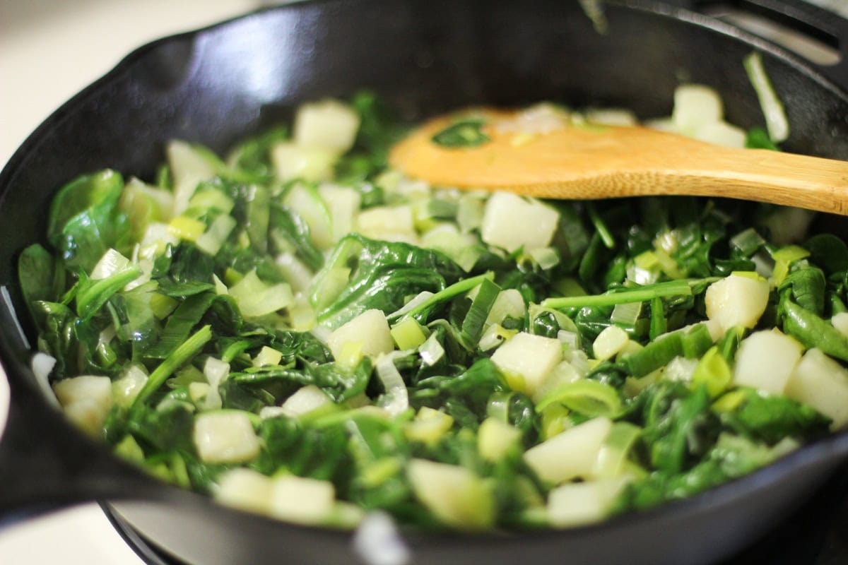 Cast iron skillet with potatoes, spinach, and leek sautรฉing.