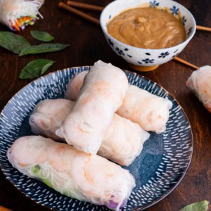 Spring rolls on a beautiful plate with a bowl of peanut dipping sauce and chop sticks to the side.