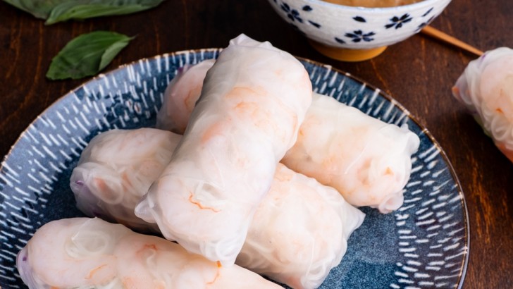 Spring rolls on a beautiful plate with a bowl of peanut dipping sauce and chop sticks to the side.