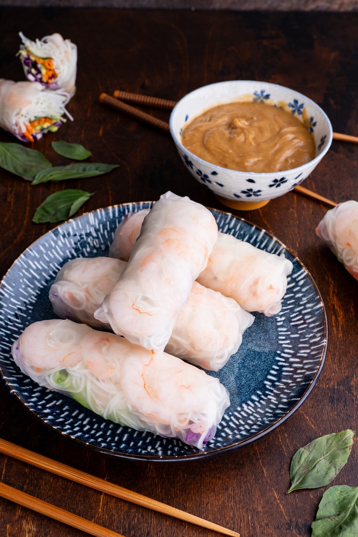 Spring rolls on a beautiful plate with a bowl of peanut dipping sauce and chop sticks to the side.